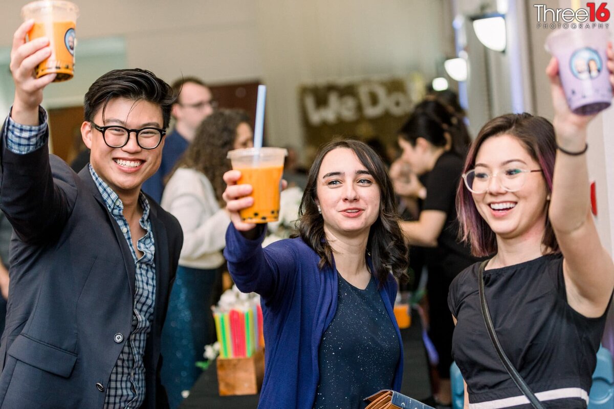 Event guests lift their boba drinks in the air to toast each other