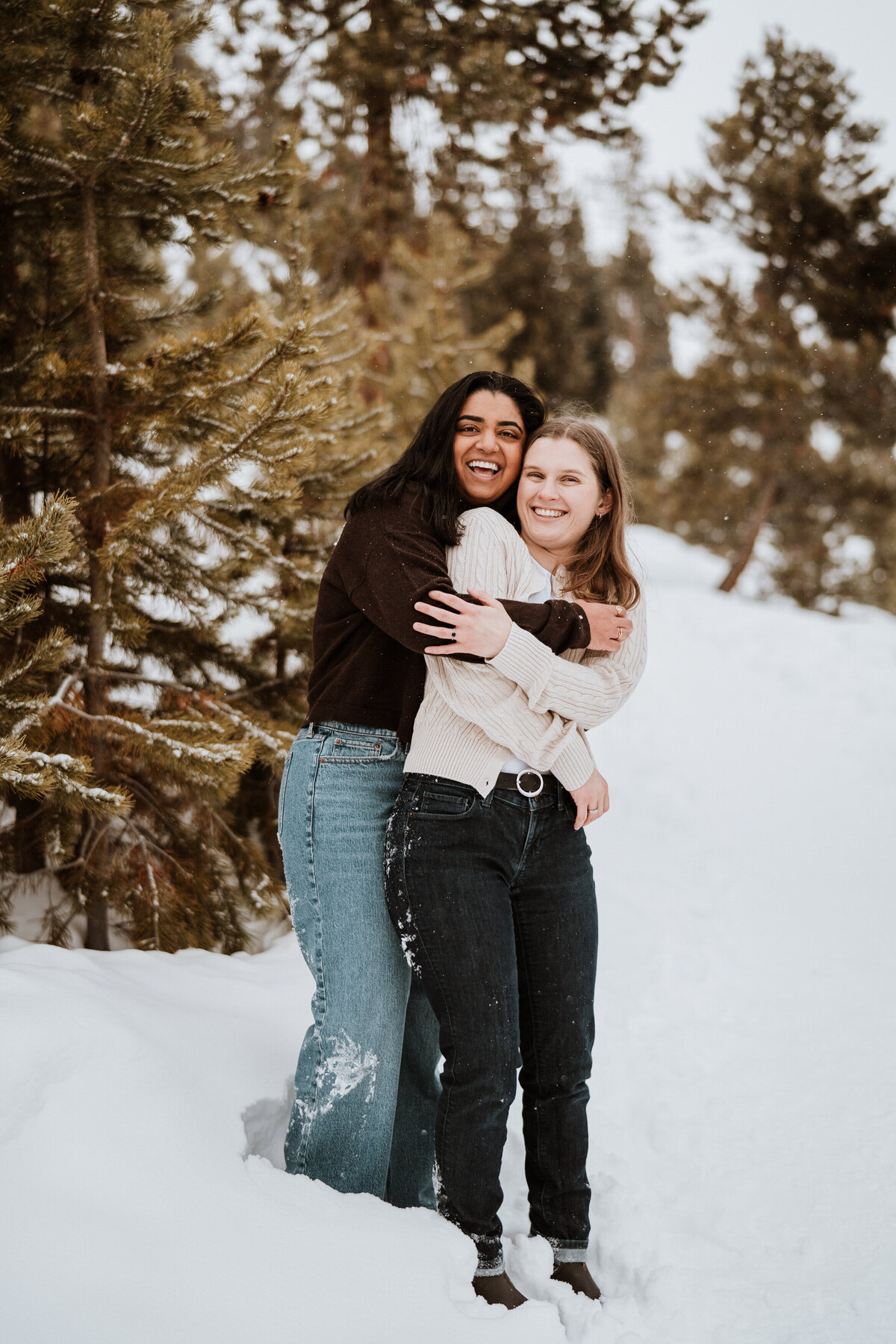 LGBTQ+ couple hugging and laughing in snowy pine forest in Sapphire Point.