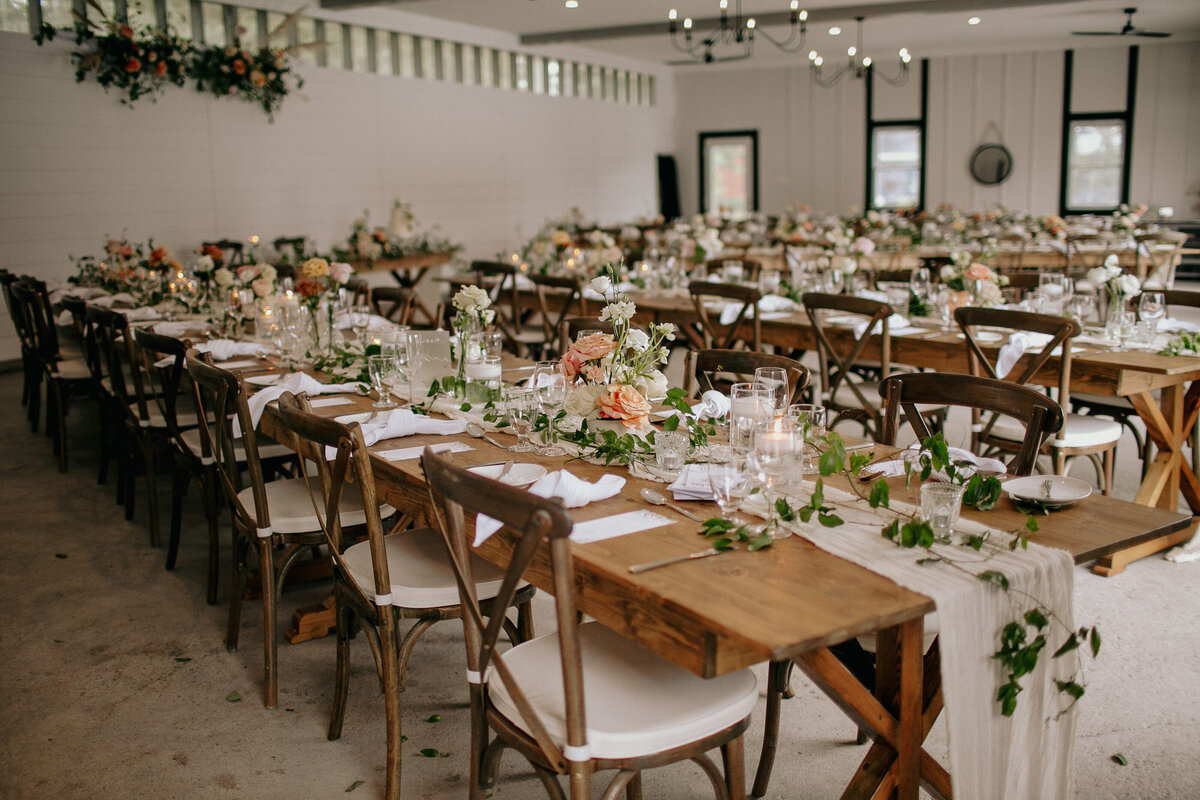 Long wood harvest tables with cheesecloth runners and peach bud vases fill the modern barn venue Bleeks & Bergamot in Almonte Ontario