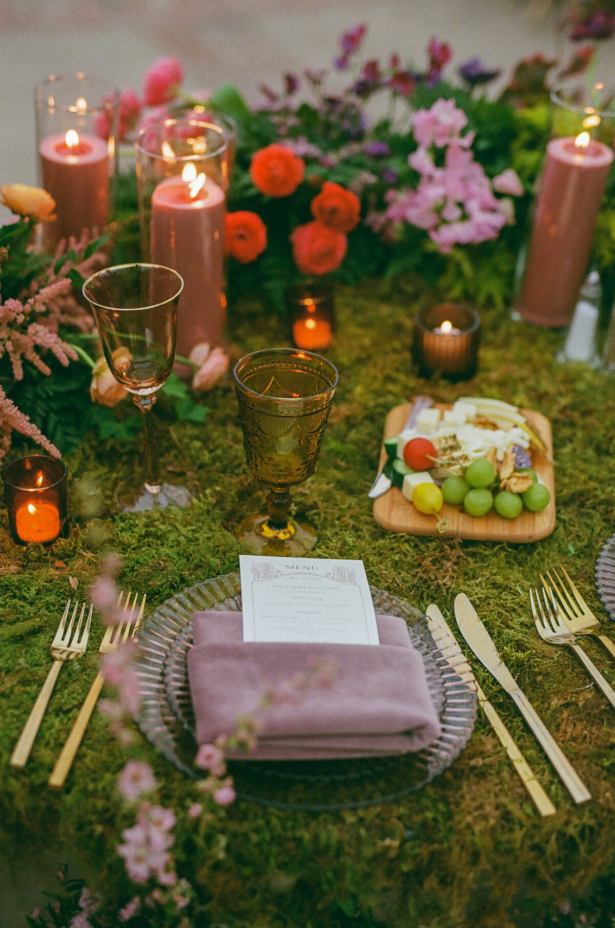 A reception table covered in moss with candles and flowers on it.