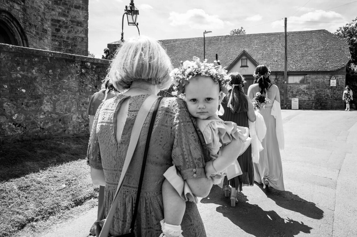 Baby flower girl looking to camera being carried buy nanny