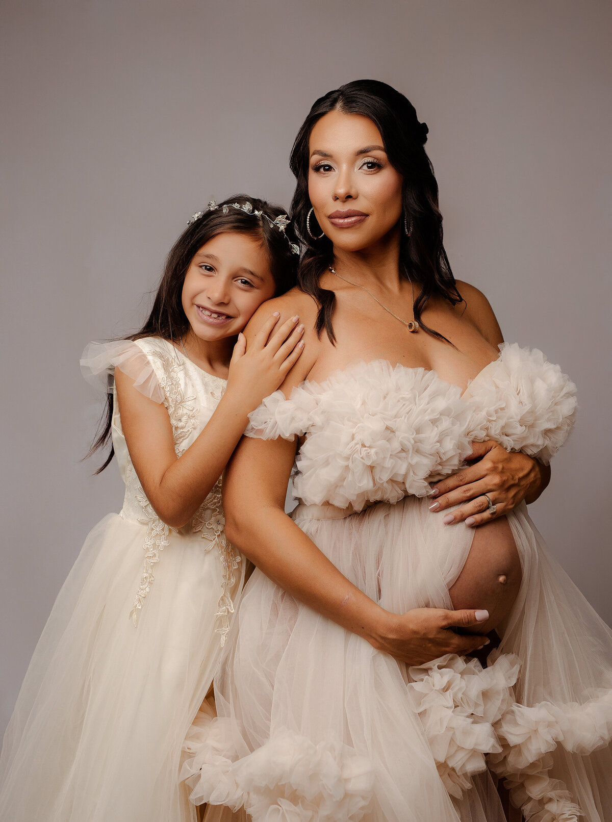 daughter holding on to pregnant mother's shoulder in white dresses