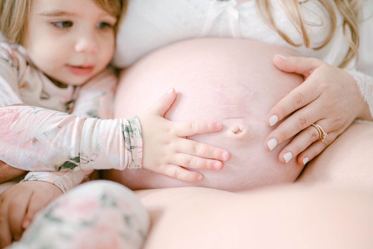 Toddler is touching and looking at growing baby bump