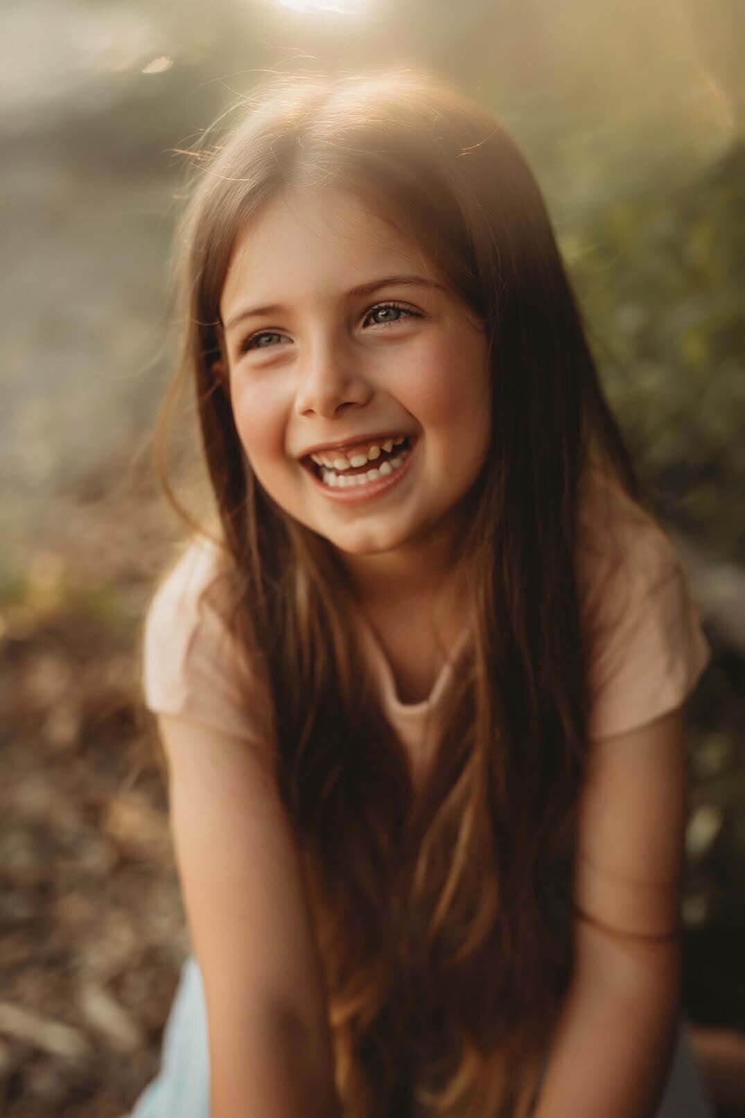 A young girl looks off into the distance with the warm sunset glowing behind her