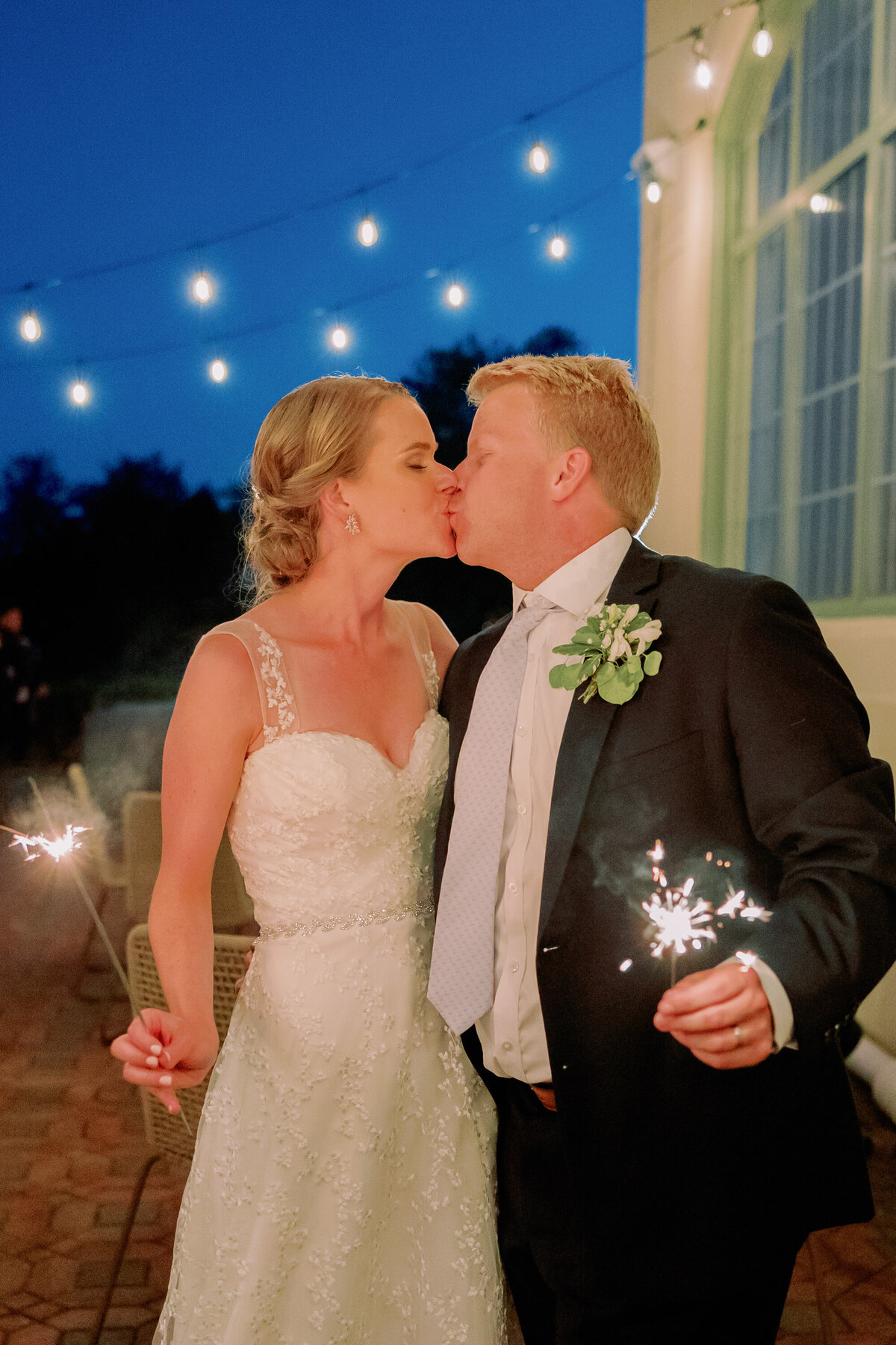 A newlywed couple kissing as they both hold a sparkler in one hand 