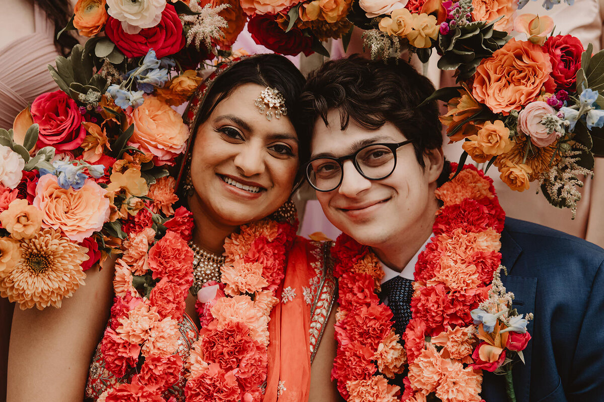 A wedding couple smiling while surrounded by flowers 