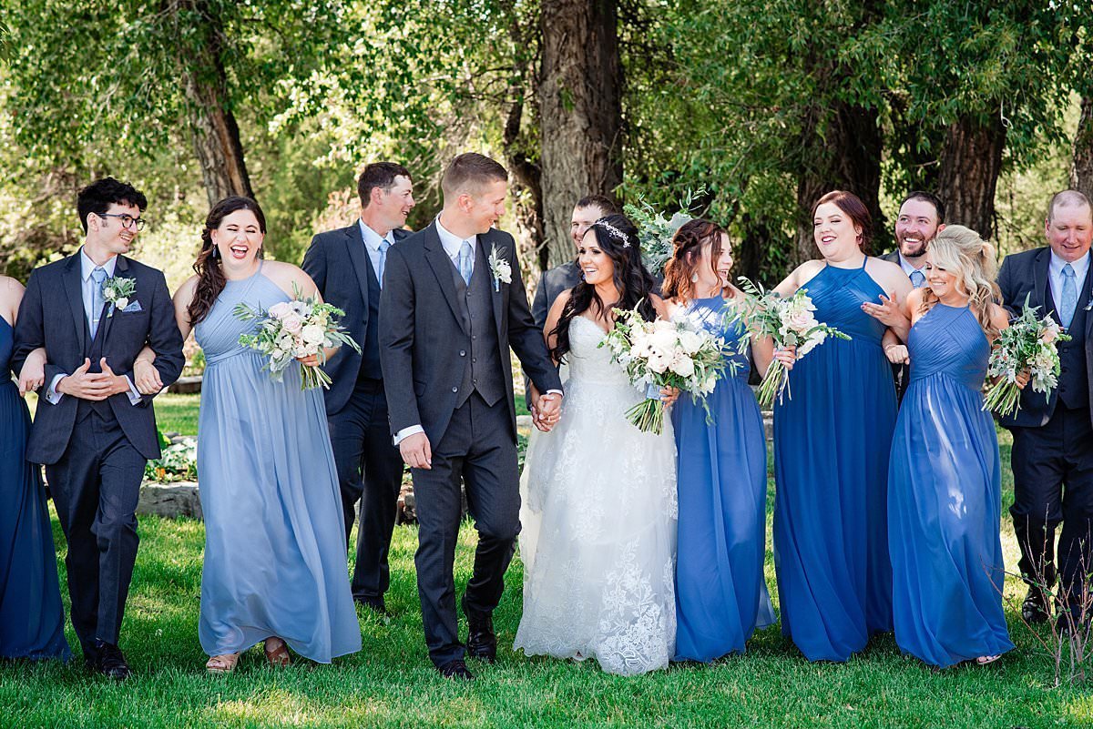 Bridesmaids wearing shades of blue and groomsmen in shades of grey walking together at Headwaters Ranch