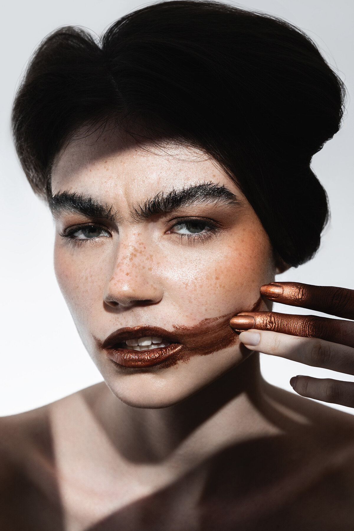 Bold beauty photography close-up of freckled model smearing metallic lipstick across face