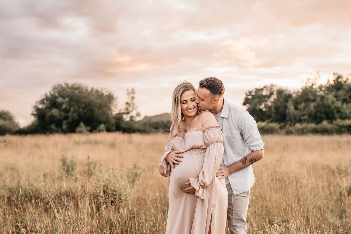 Photo of a pregnant woman sanding with her husband in a field of long grasses