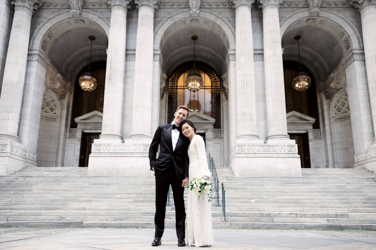 The bride and the groom are smiling in front of the New York Public Library's grand entrance. Image by Jenny Fu Studio