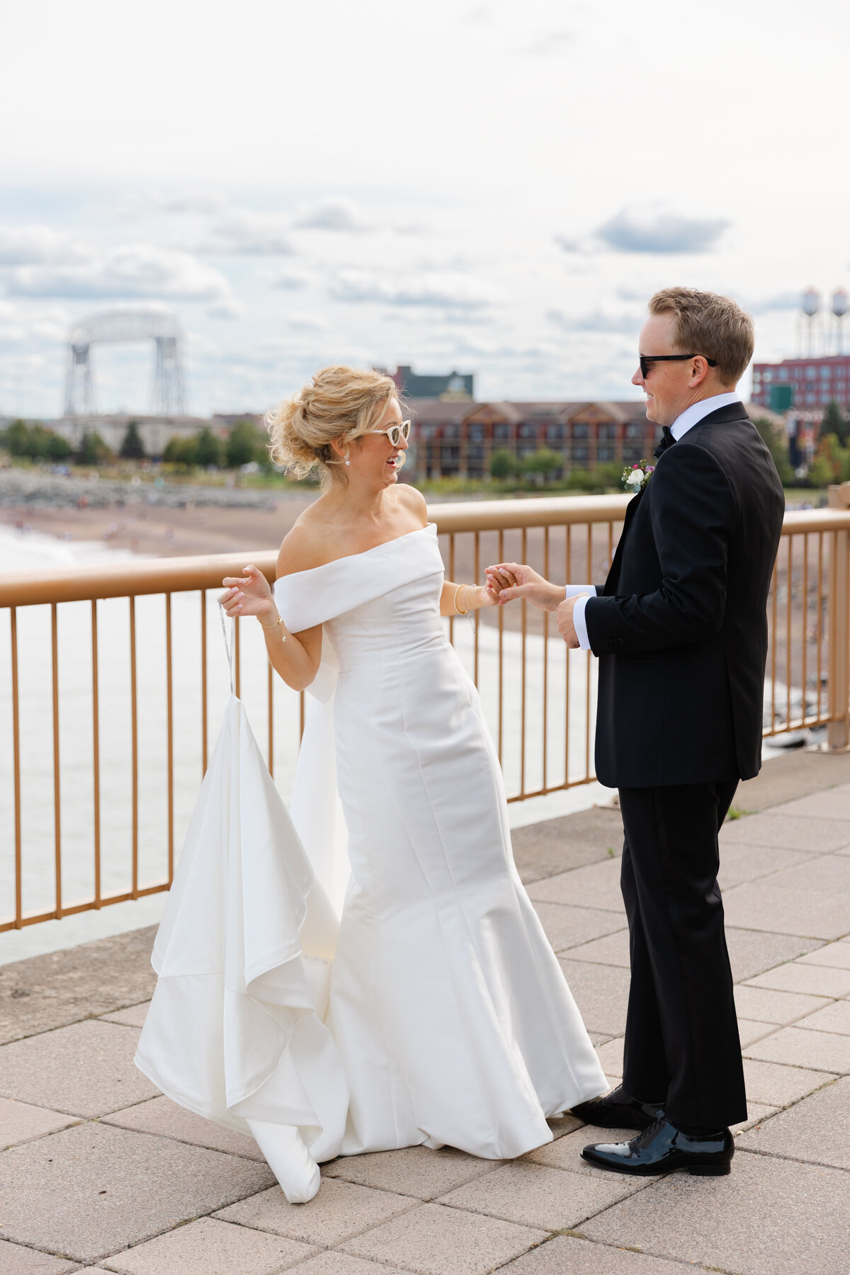 Overlooking Canal Park and the Lift Bridge, a newlywed couple smiles at each other.