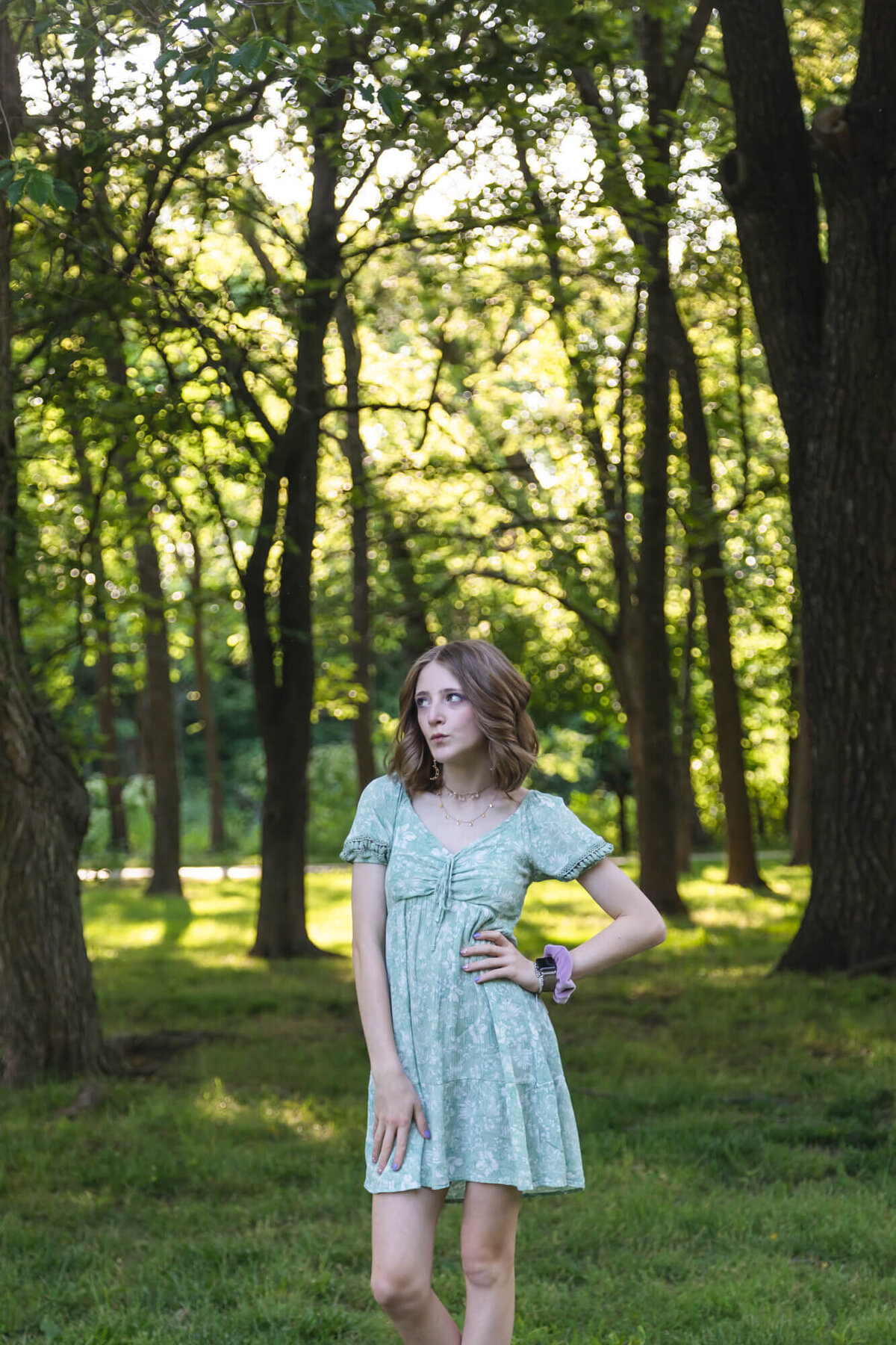 A young blonde teen girl in a green floral dress striking a pose in the park. Captured by Springfield, MO teen photographer Dynae Levingston.