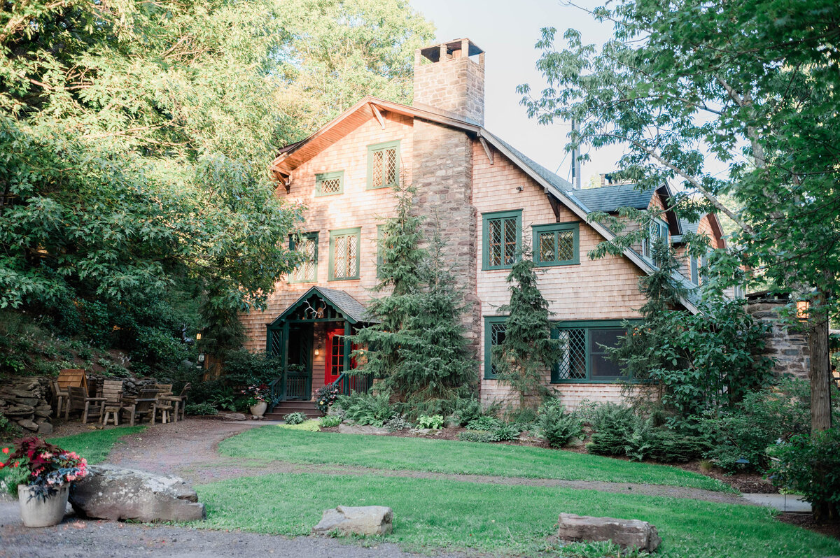 A charming rustic inn with stone and wood siding, covered in green plants, with a mowed lawn and a welcoming red door.