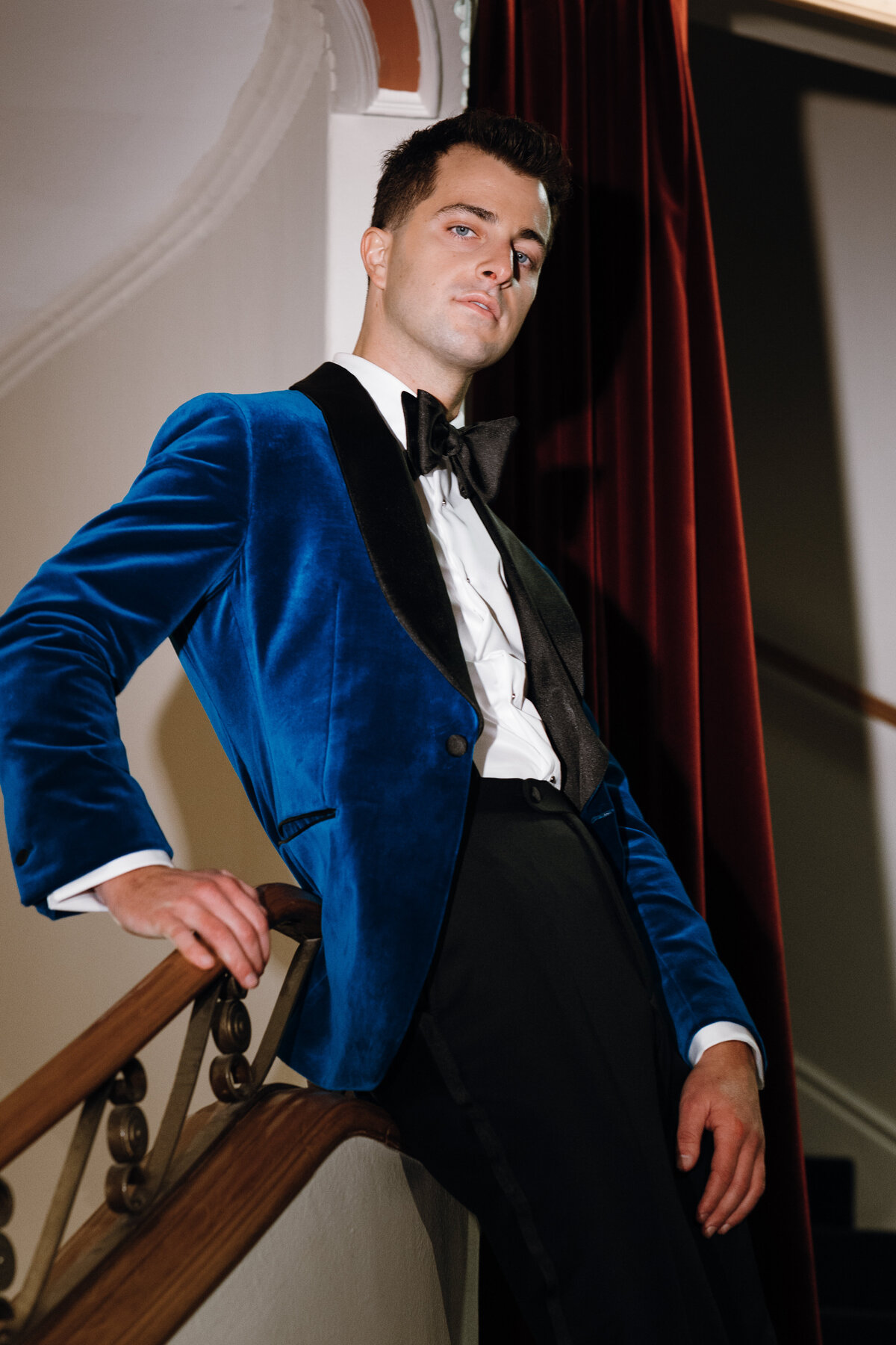 Close up image of a groom posing against the hand rail of a staircase.