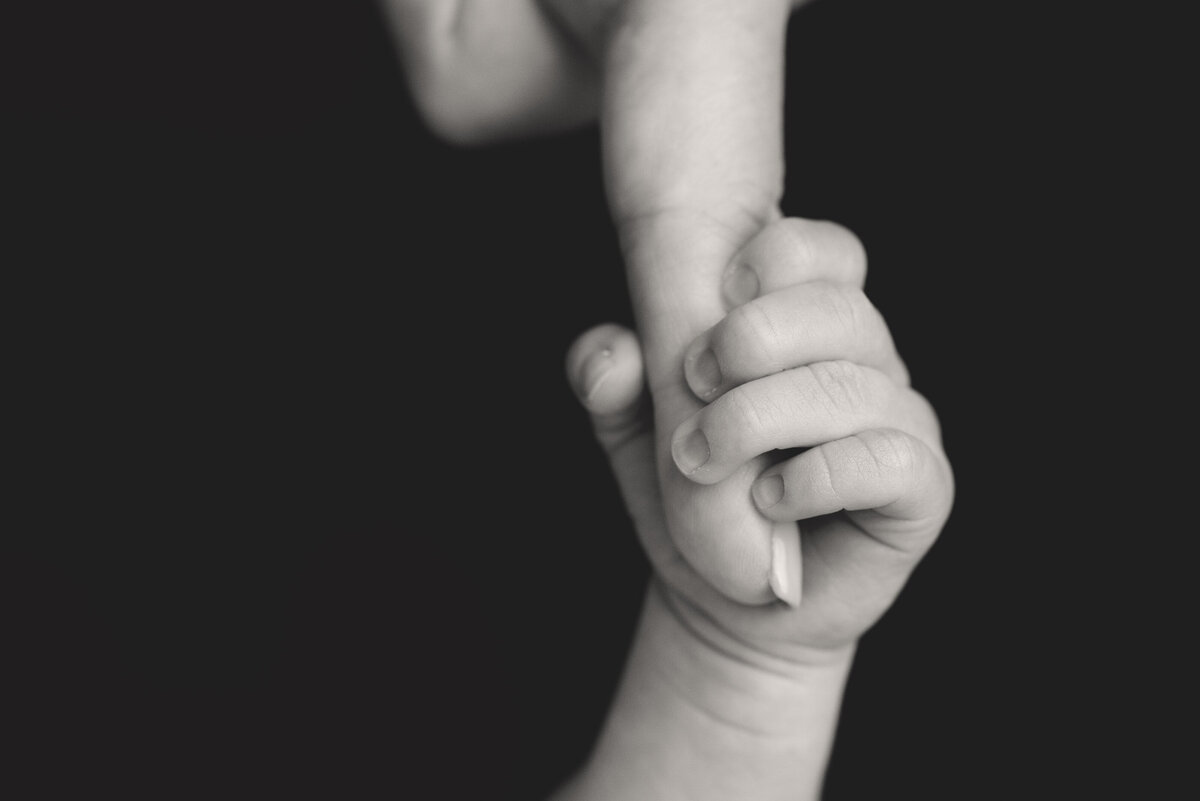 Black and White image of newborn baby holding  Moms finger.