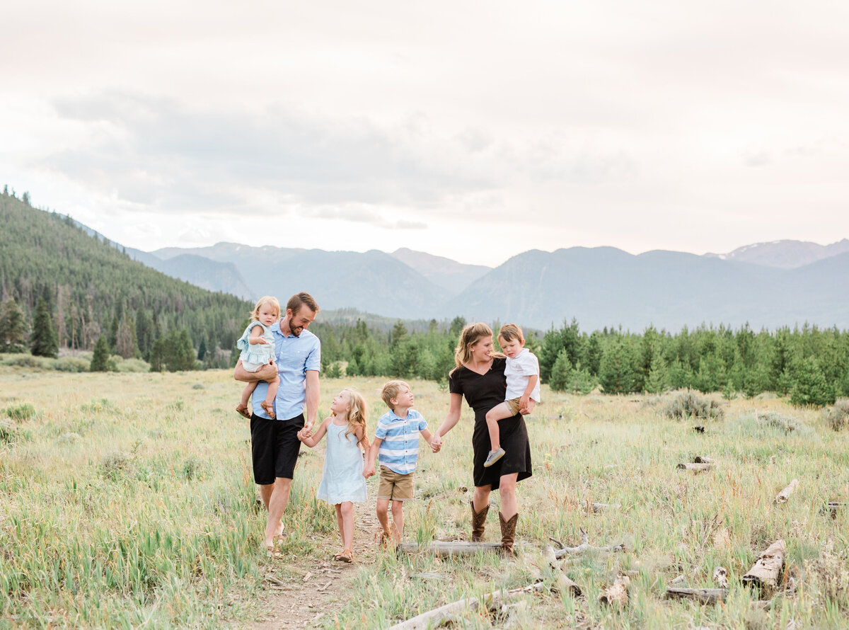 A family of six walks hand in hand through a grassy mountain field