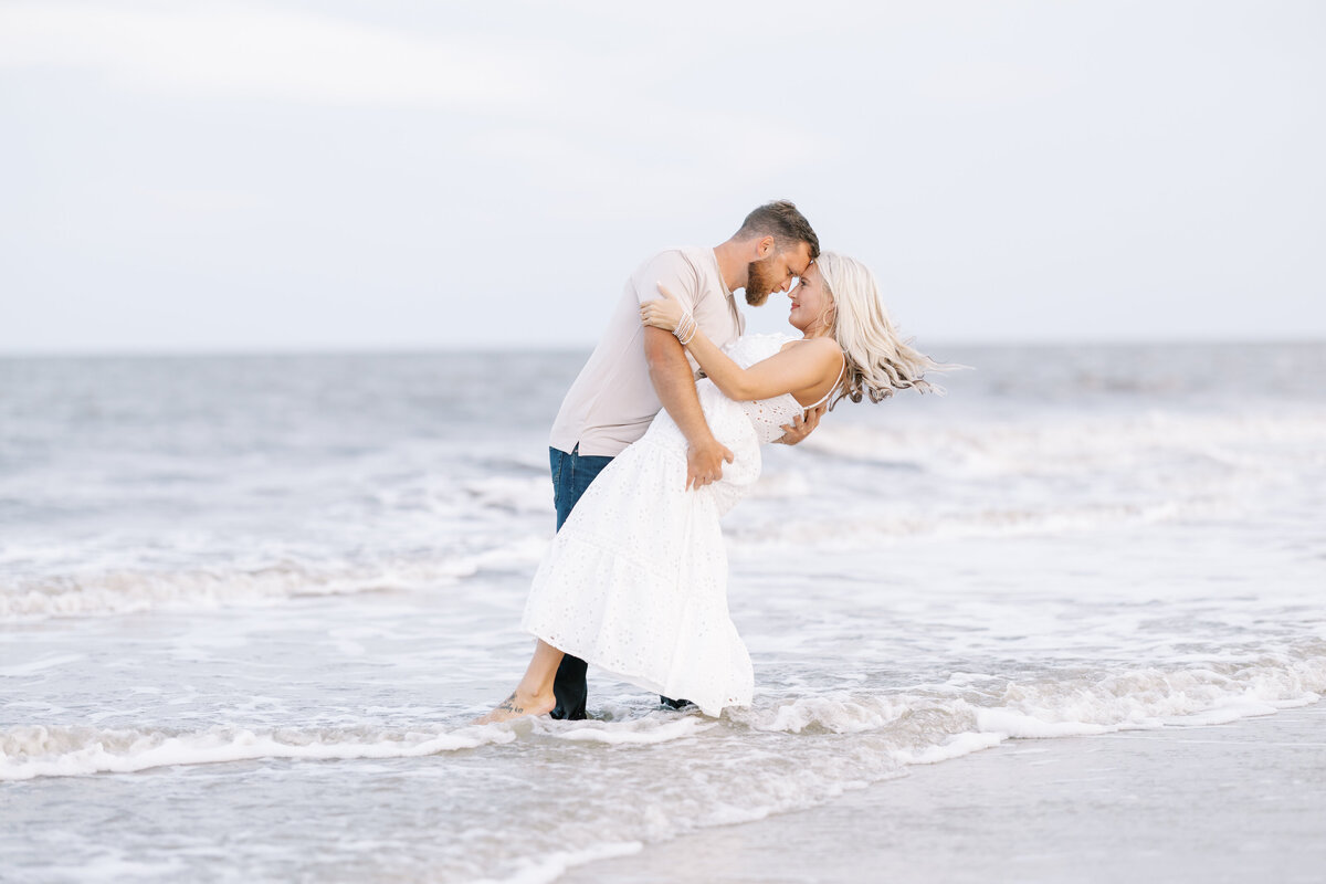 a man dipping his fiance as they stand in shallow ocean waves