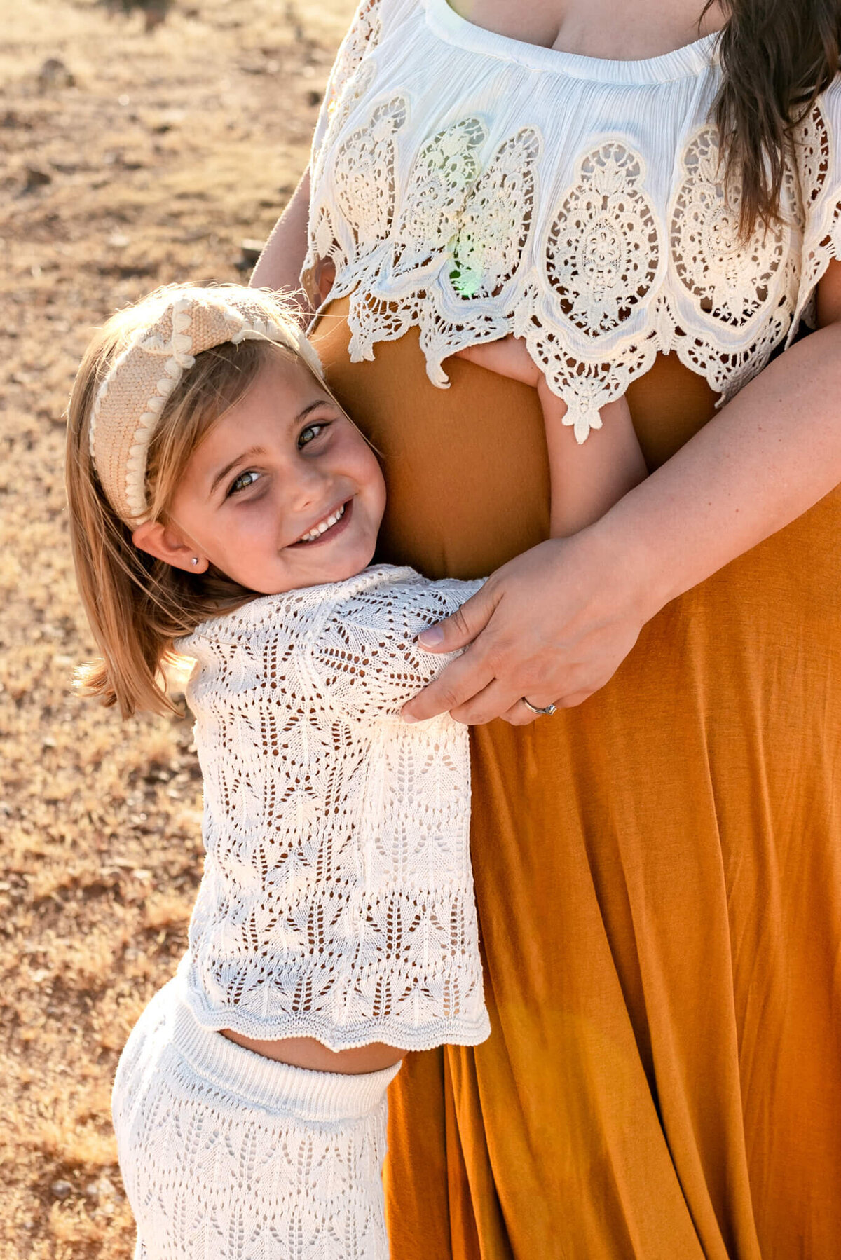 Young daughter smiling and hugging her pregnant mom's belly in Arizona desert
