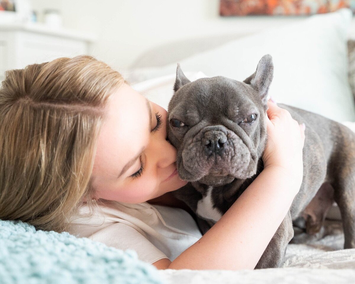 A woman lovingly cuddles her French Bulldog on a cozy bed during an in-home session by Calgary pet photographer Chase Magic Photography.
