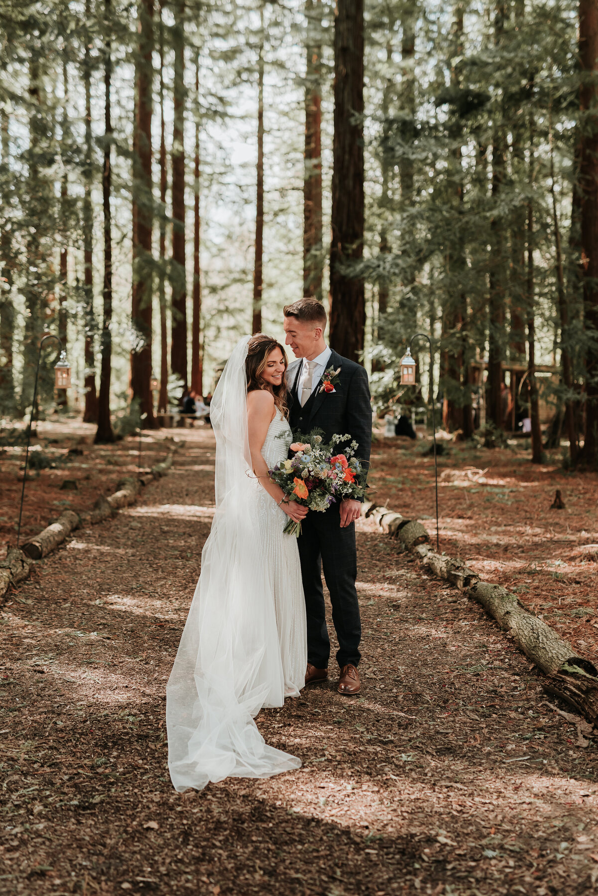 Bride & Groom standing along a woodland pathway holding a rustic wedding bouquet at their intimate woodland wedding at Two Woods Estate