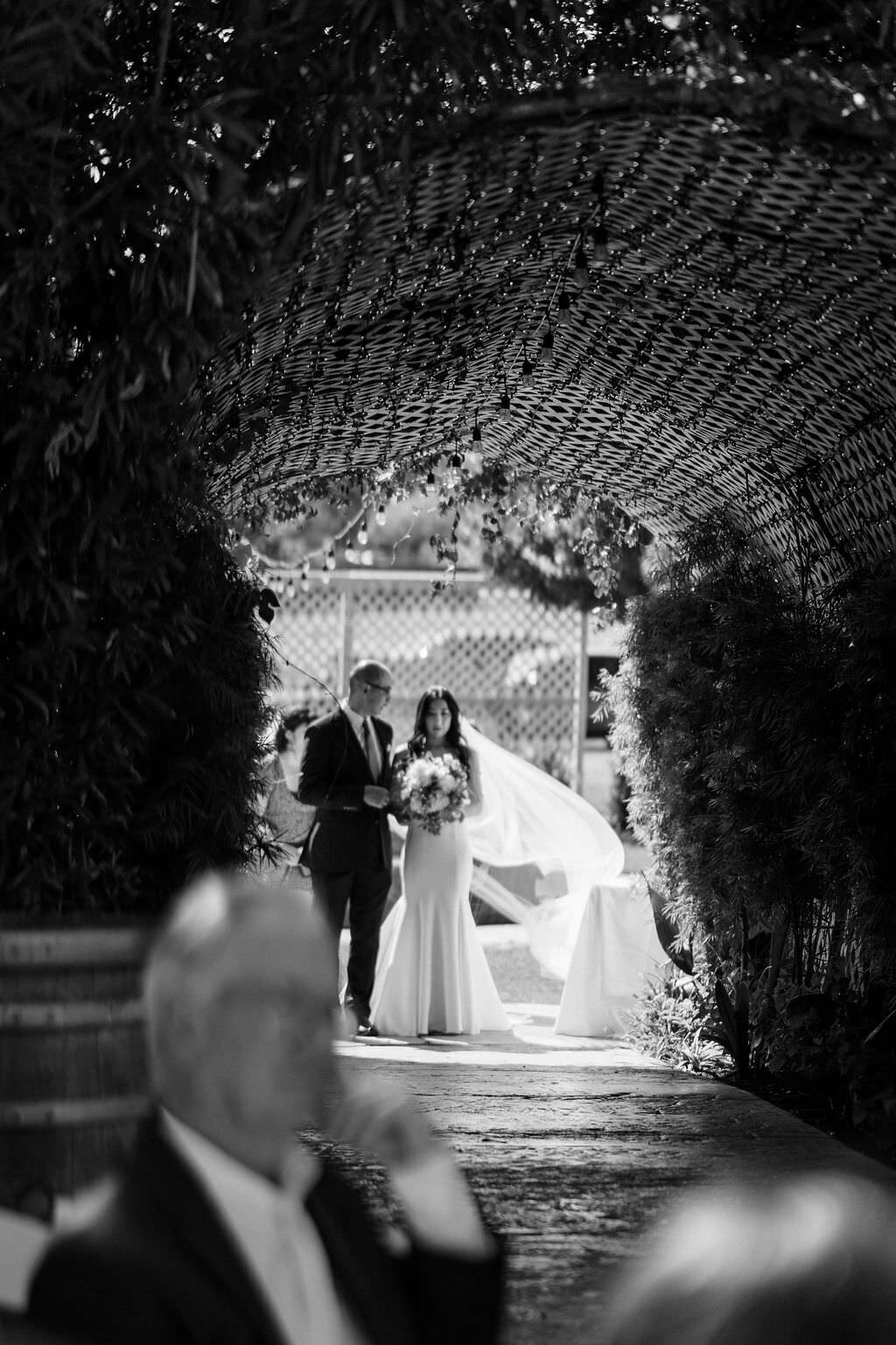 black and white photo of a father walking his daughter down the aisle while guests look on
