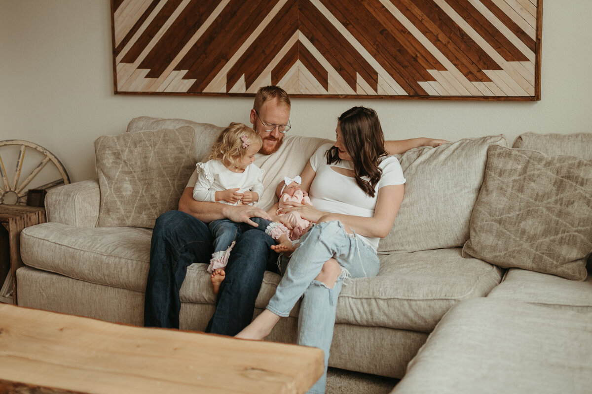 family of four sitting on couch in longmont colorado looking at newborn baby during in home newborn session with alexis adkins photography