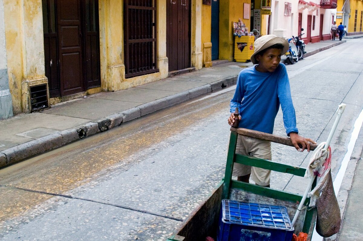 A boy leans on a cart on a mostly empty street in Cartagena Columbia.