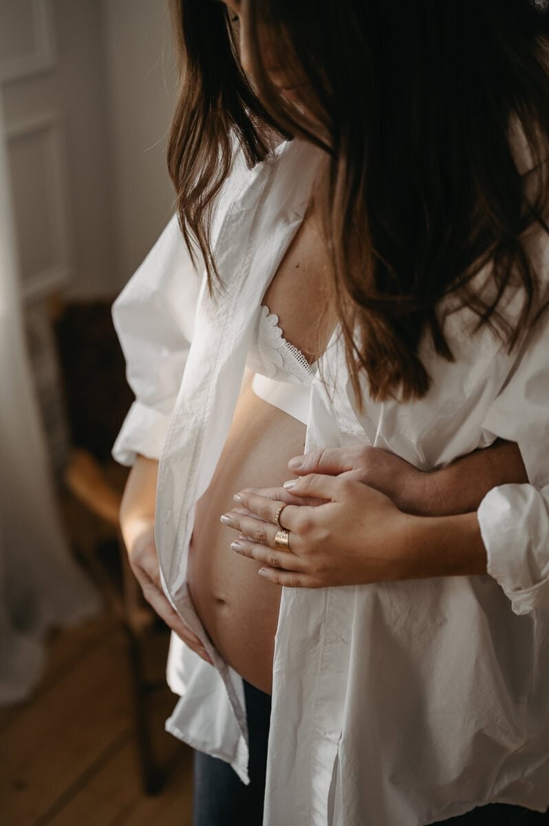 Gravid kvinna har öppen skjorta så gravida magen blottas och mannens händer håller om magen.