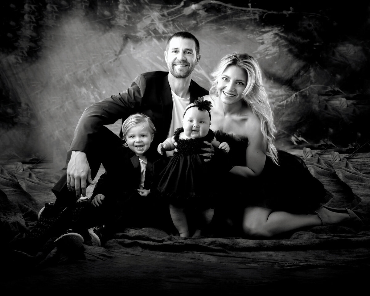 Family of 4 sit together and smile for their B&W Iowa Family Pictures