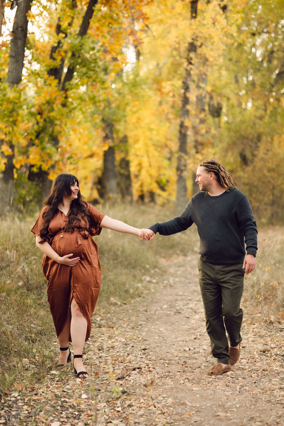 A couple holds hands and walks during their Maternity Session at Riverbend Ponds in Fort Collins, Colorado.