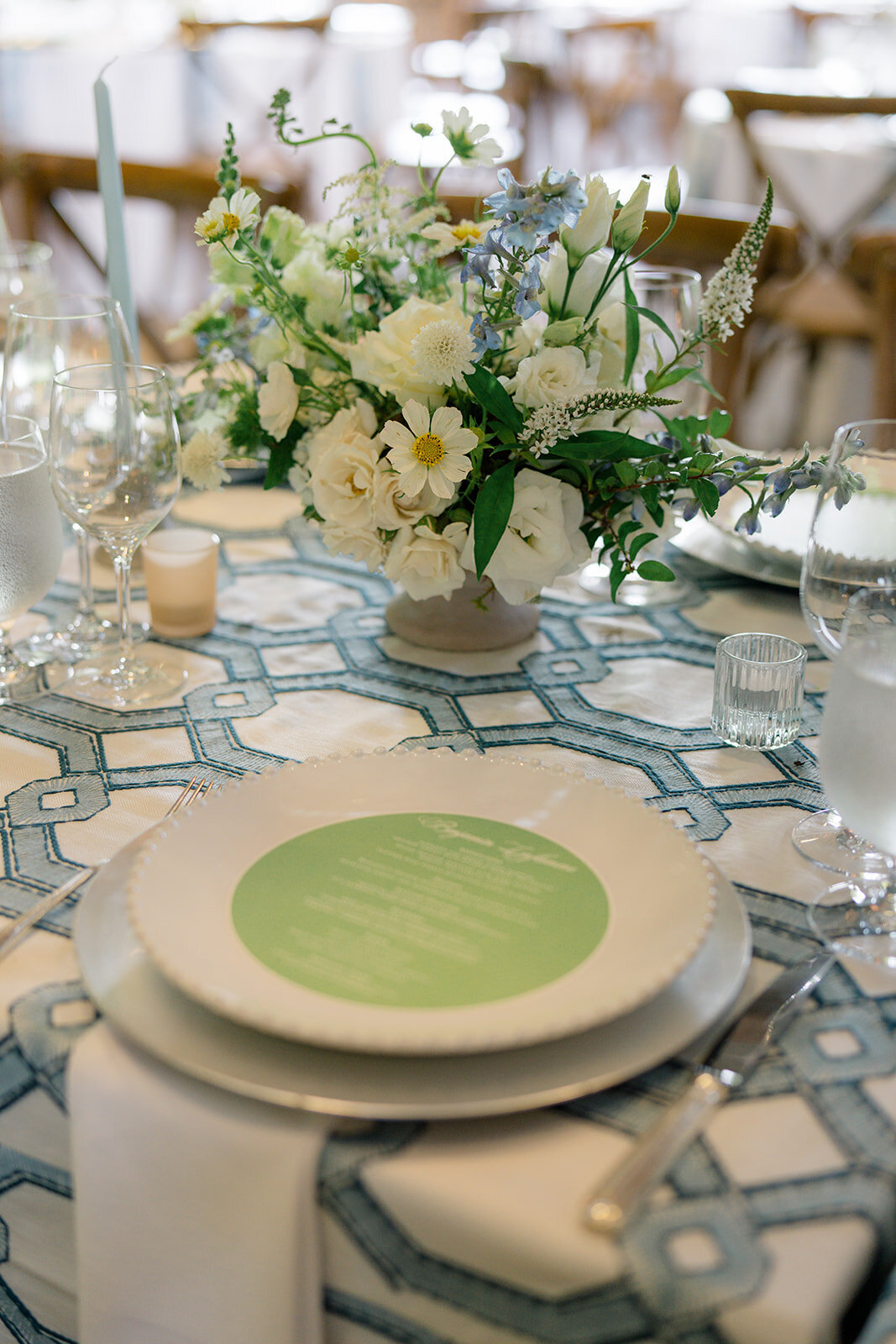 Blue patterned linen with white floral centerpiece and green menu on charger plate at spring wedding reception.