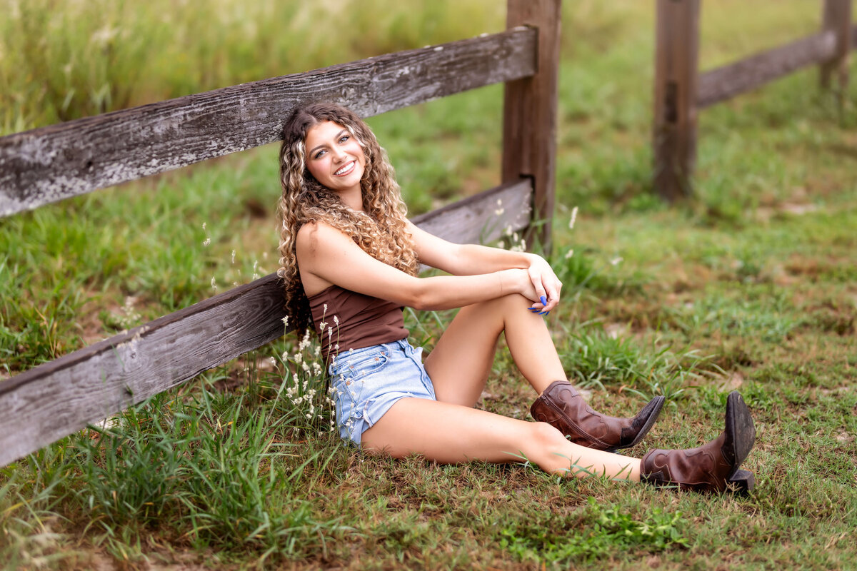 Playful Winter Garden senior pictures with a teen girl posing on a rustic fence.