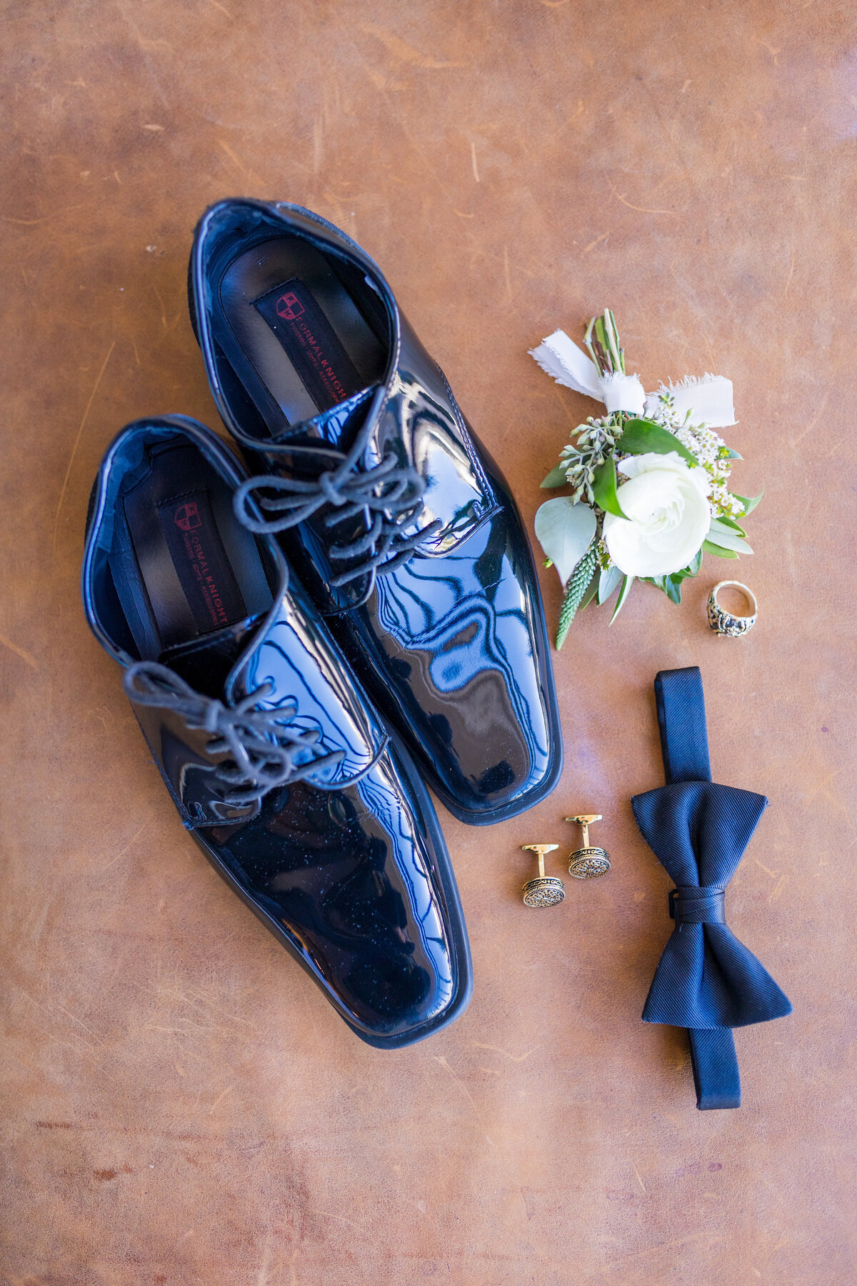 A collection of groom's details including his shoes, bow tie, ring, cuff links, and boutonniere.