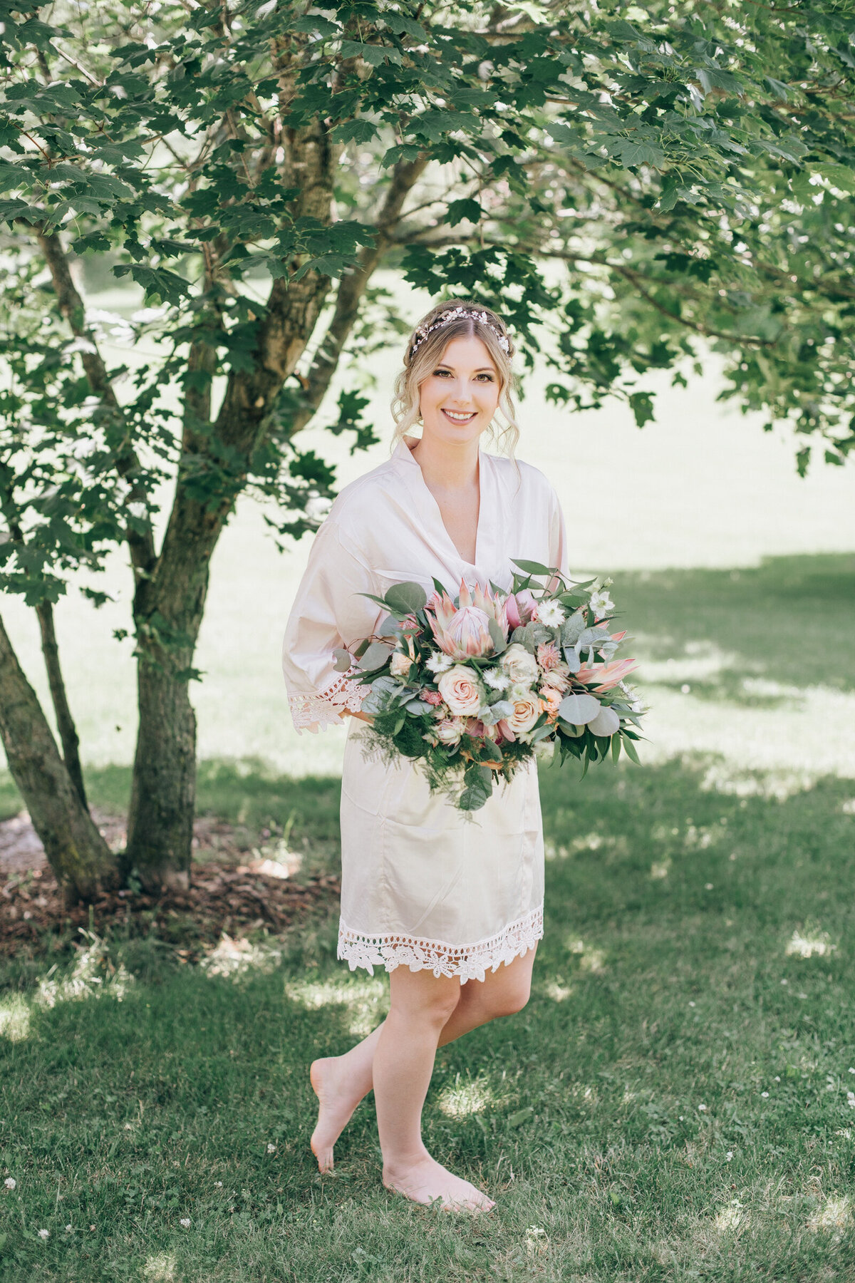 A bride in a pink robe posing with her big, whimsical wedding bouquet