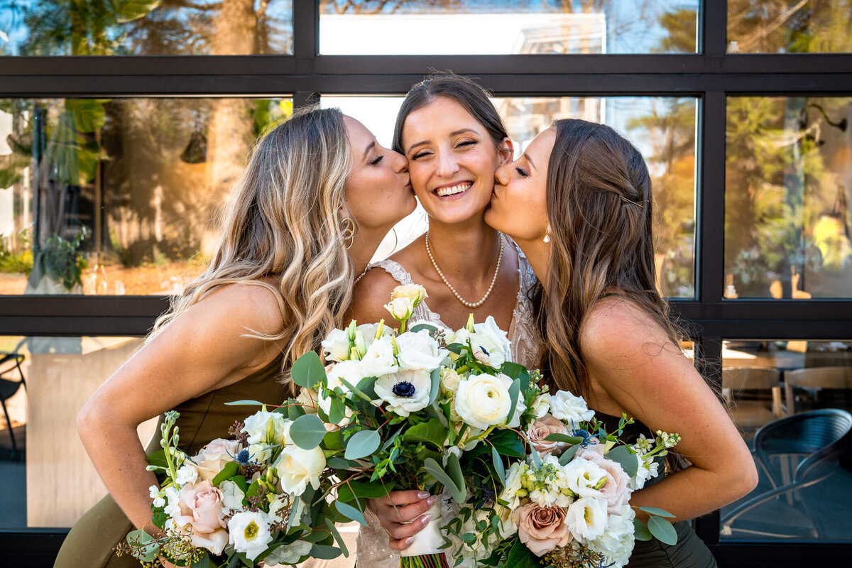pittsburgh wedding photography of bride being kissed on her cheek by both of her sisters while smiling. Captured by Pittsburgh Wedding Photographer Michael Fricke Photography.