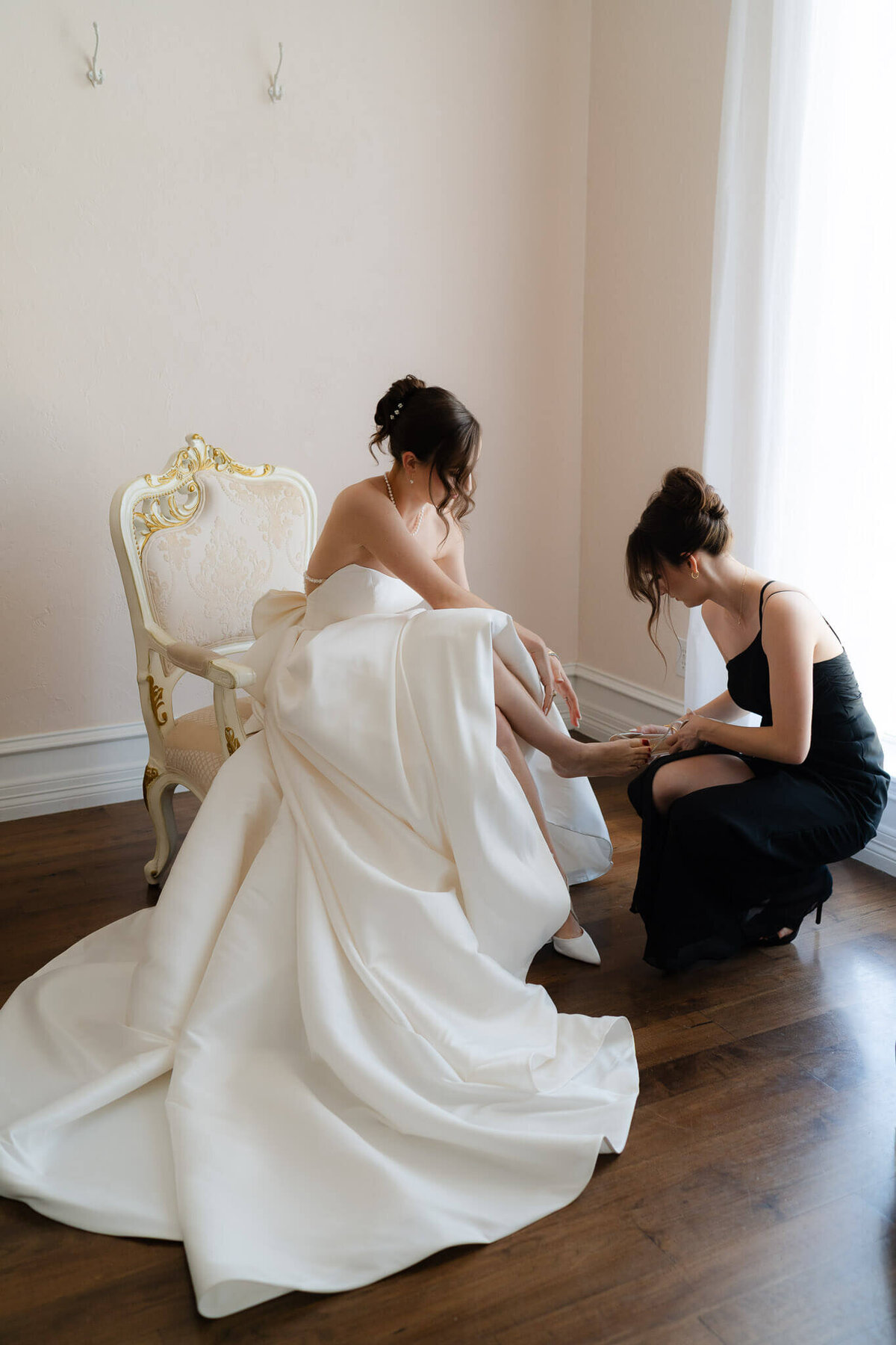 in a gorgeous bridal suite,  bride's sister helps to put her shoes on