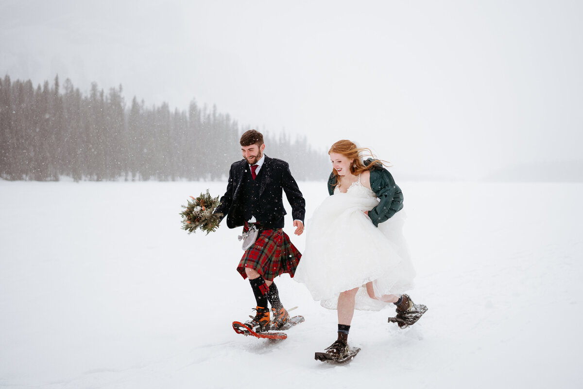 Couple runs together in snowshoes during winter Emerald Lake elopement