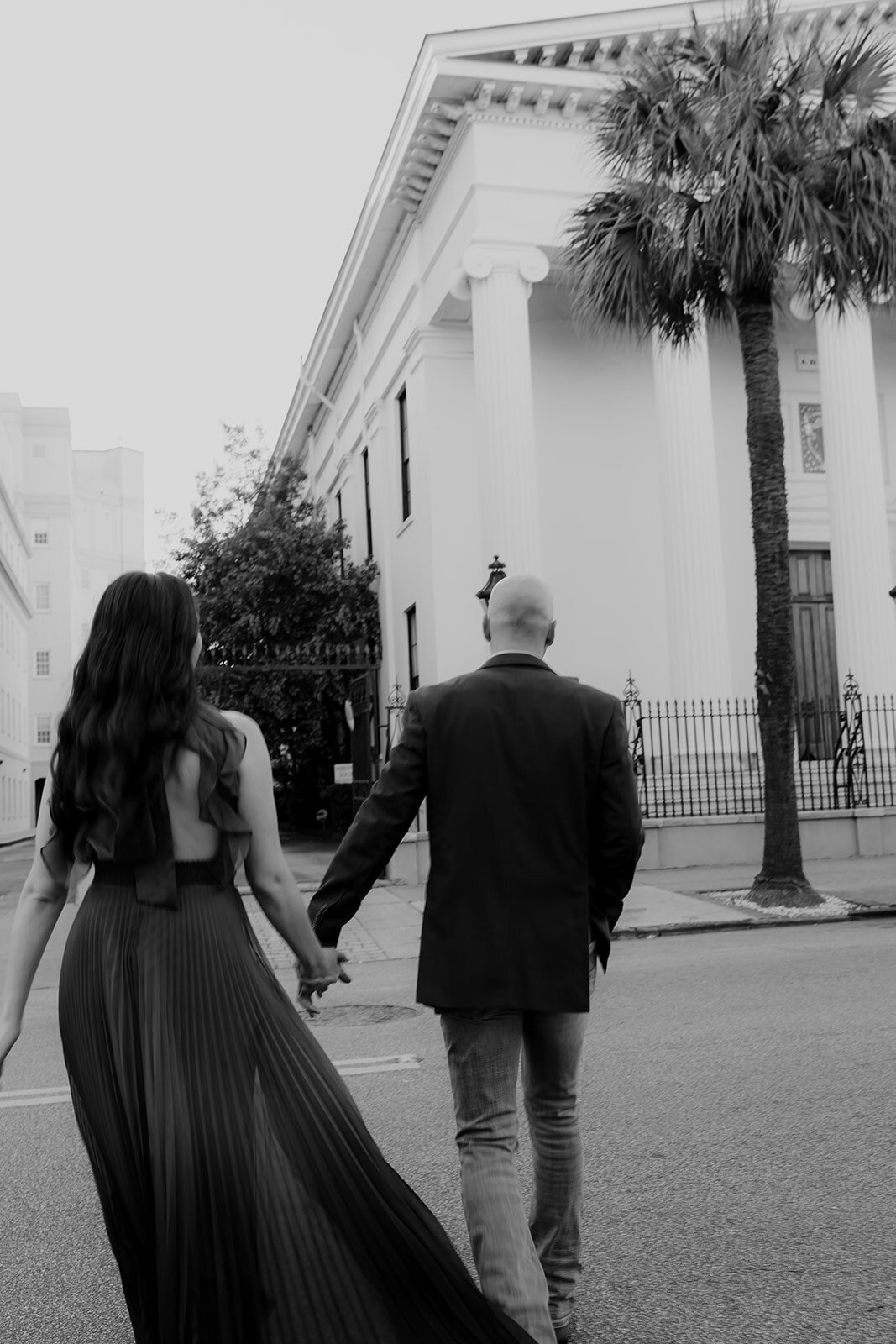 Couple holding hands while crossing street at Hibernian Hall in CHarleston for engagement photo session