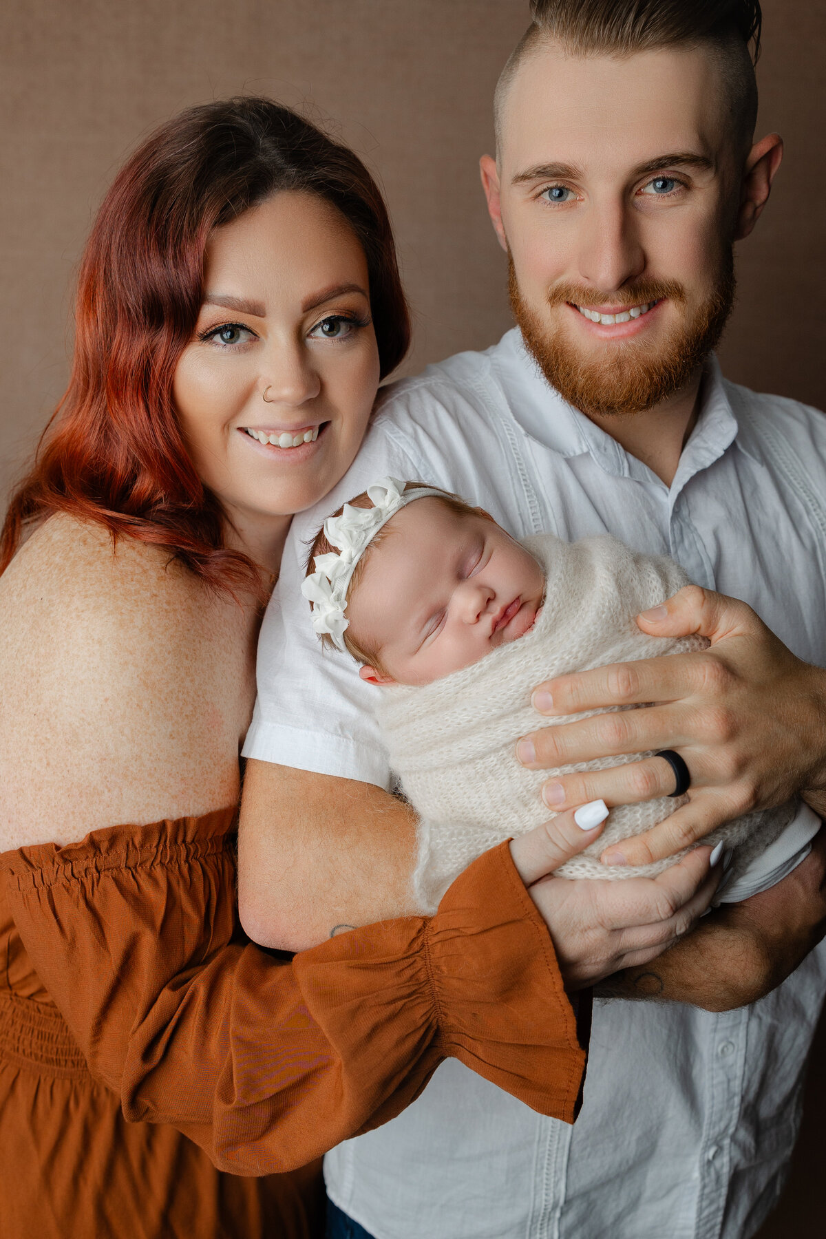 Mom and dad holding their newborn baby girl swaddled in cream with a lace bonnet during their studio session. Captured by Inland Empire newborn photographer Kaitlyn Dawn Photography.