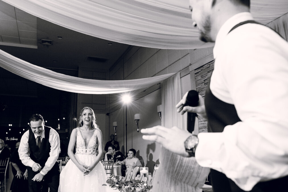 A bride and groom laughing during a speech at their wedding.