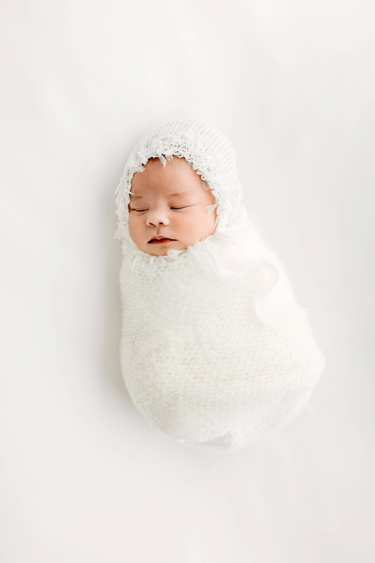 All white background and newborn baby in bonnet near Eau Claire, WI by Luci Levon Photography