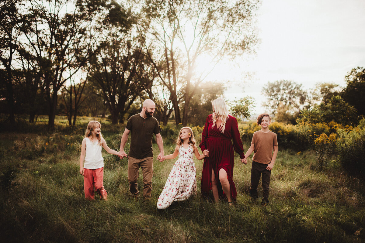 A family of five holding hands in a straight line and looking at each other