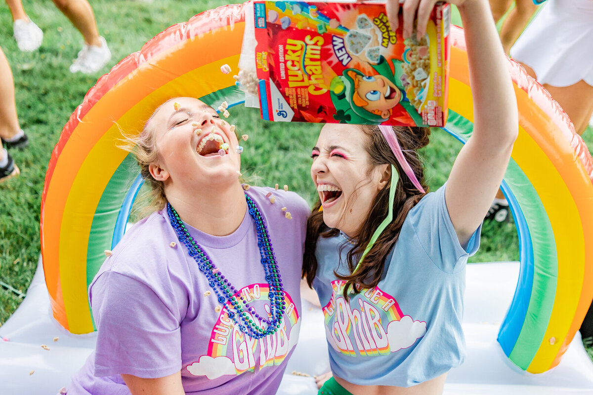 2 sorority girls with lucky charms pouring cereal into each other's mouths