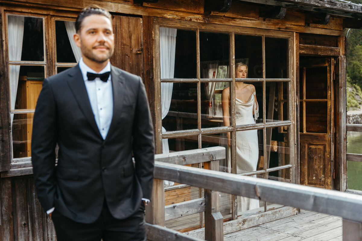 Groom in tuxedo waiting on boathouse deck at Lago di Braies