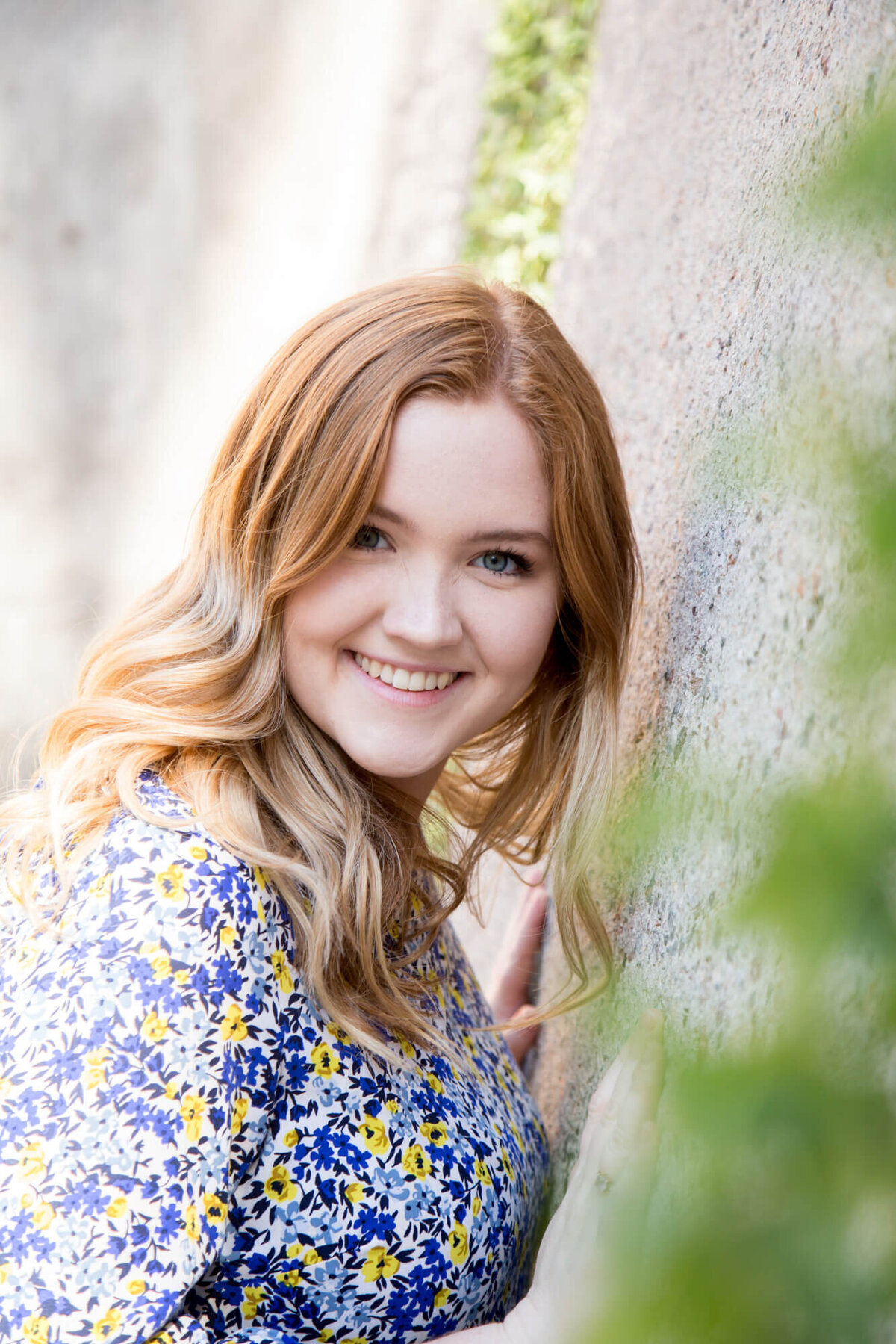 Senior girl leaning against a stone wall smiling