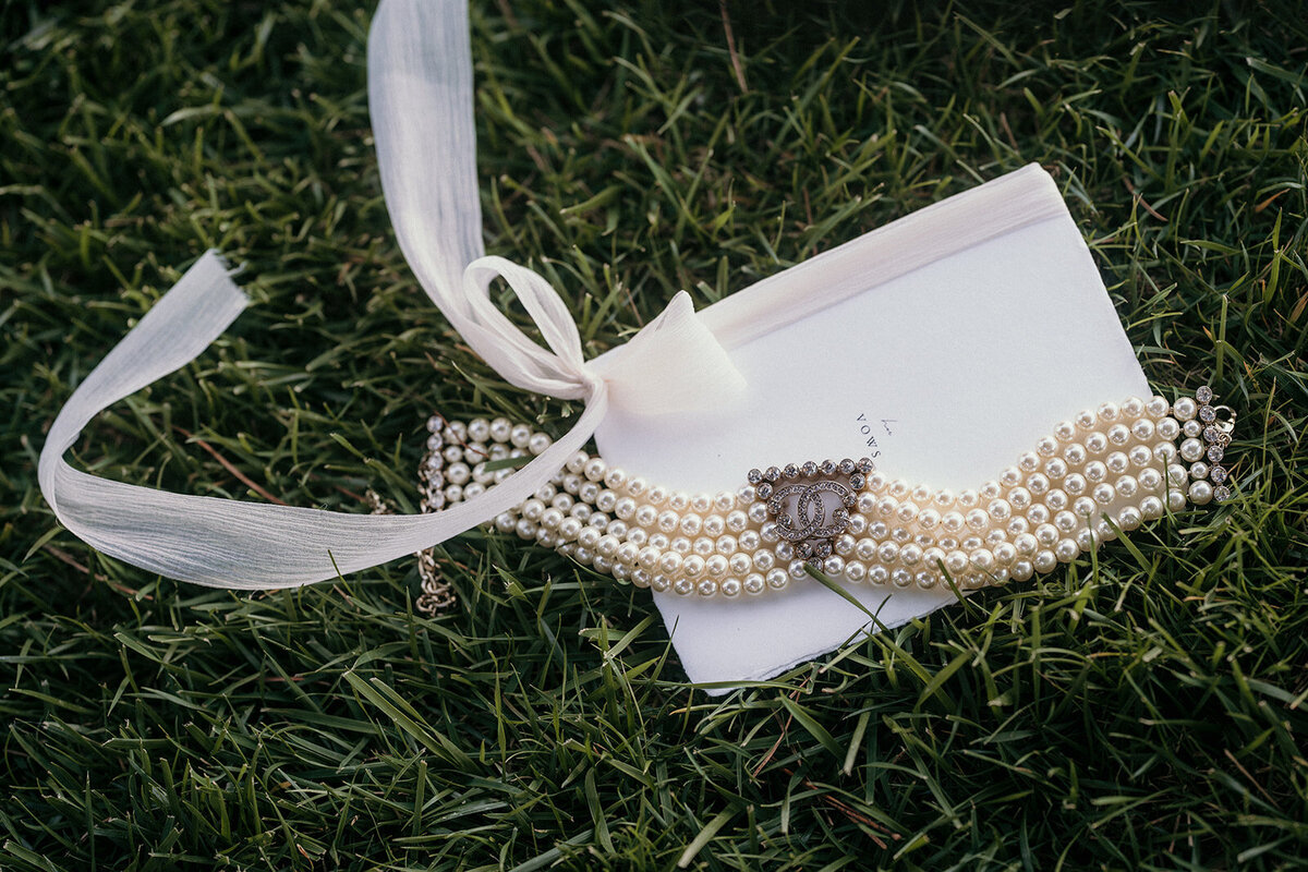 The wedding vows and the brides necklace lay on gras.