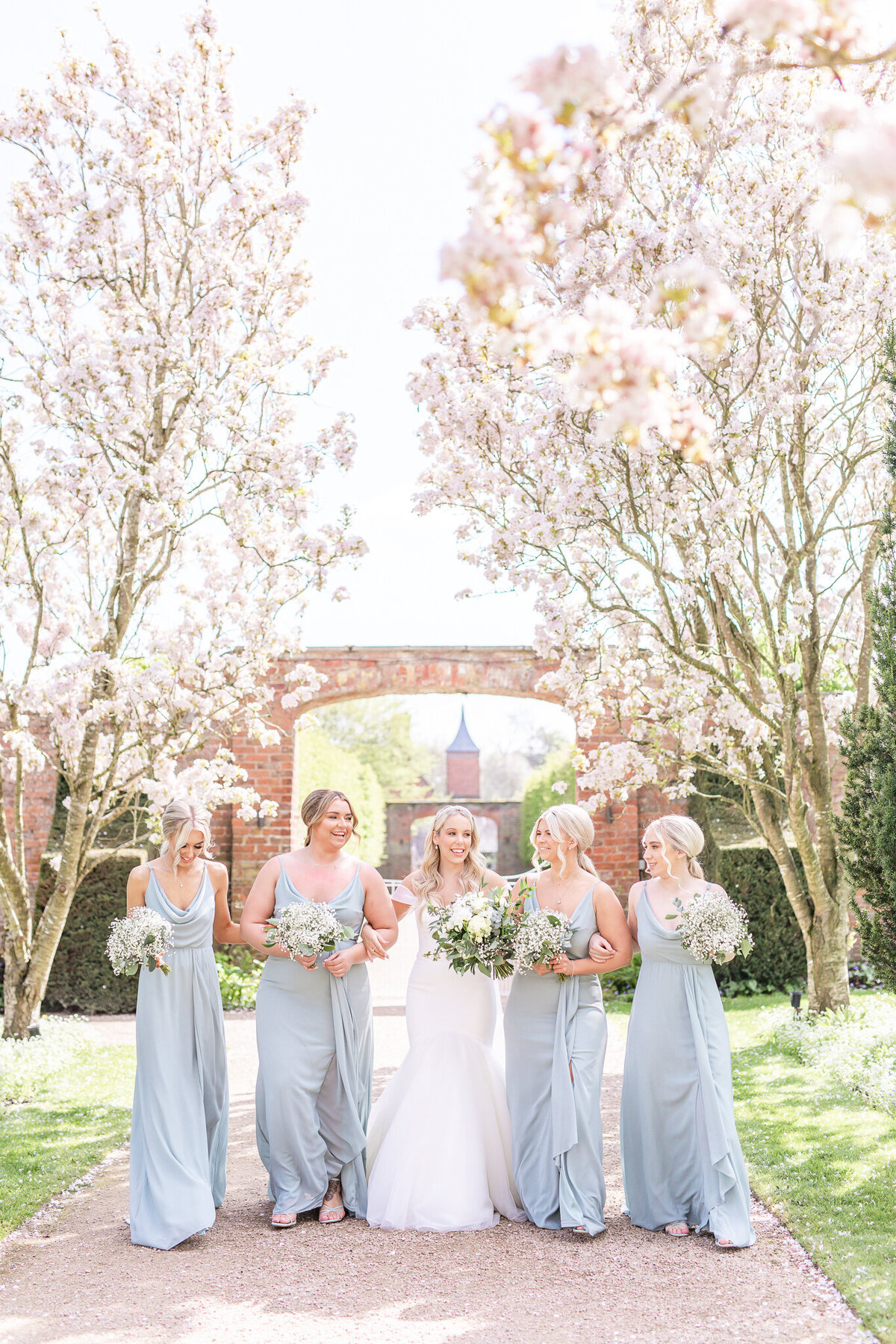 Bride and four bridesmaids linking arms walking in the grounds at Combermere Abbey