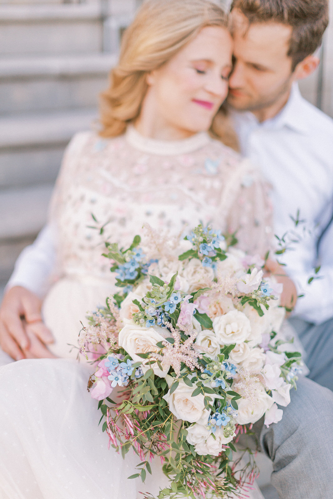 Expecting mother sits and leans into her husband as she holds a bouquet of flowers.