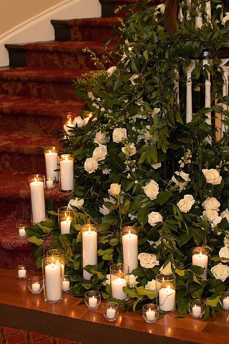 Greenery with off-white roses and lighted candles lining staircase at University Club in Pittsburgh, PA