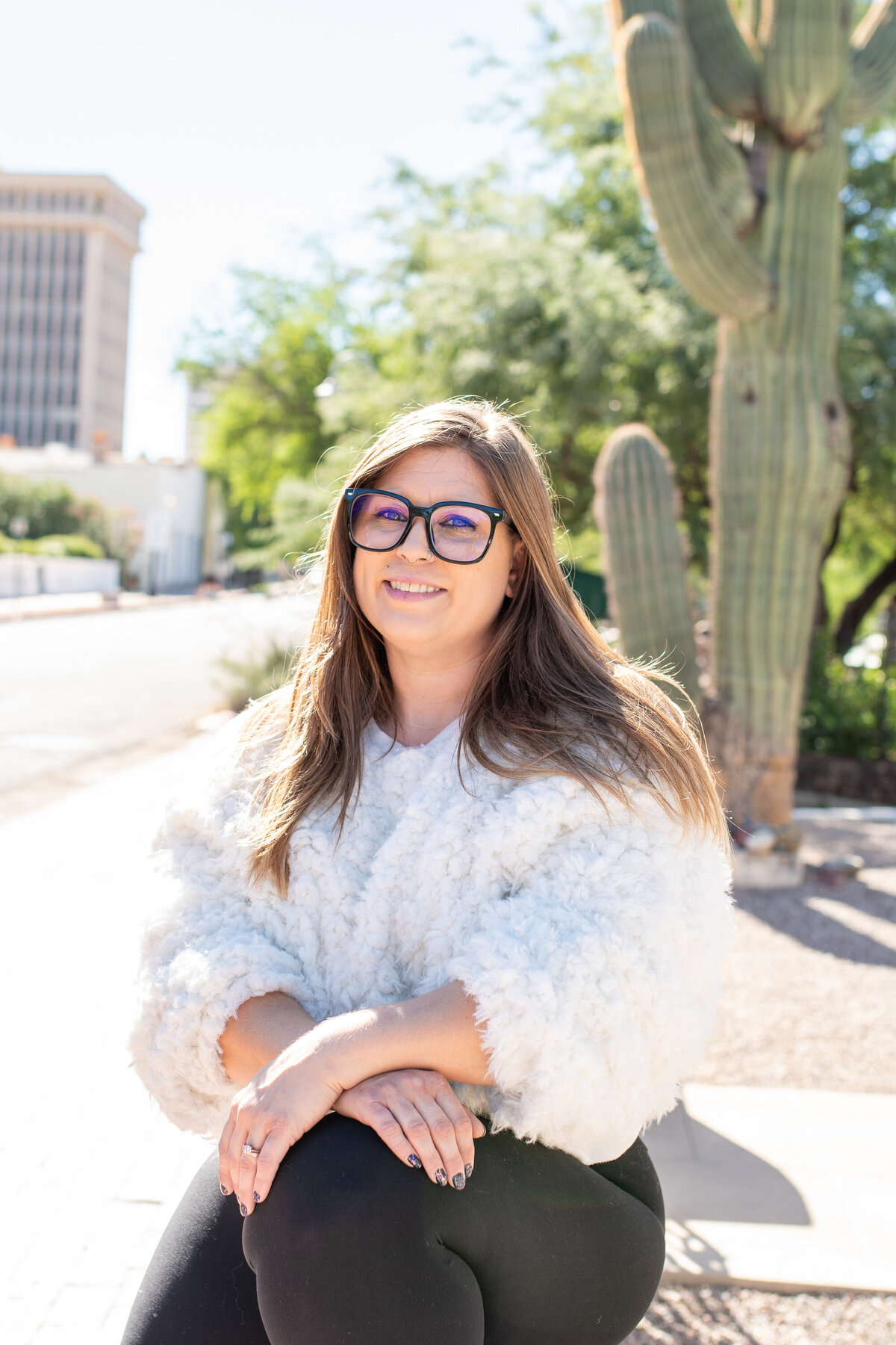 Smiling woman standing outdoors in front of desert plants and a large cactus, photographed by Vyrl Photo, showcasing Tucson brand photography.